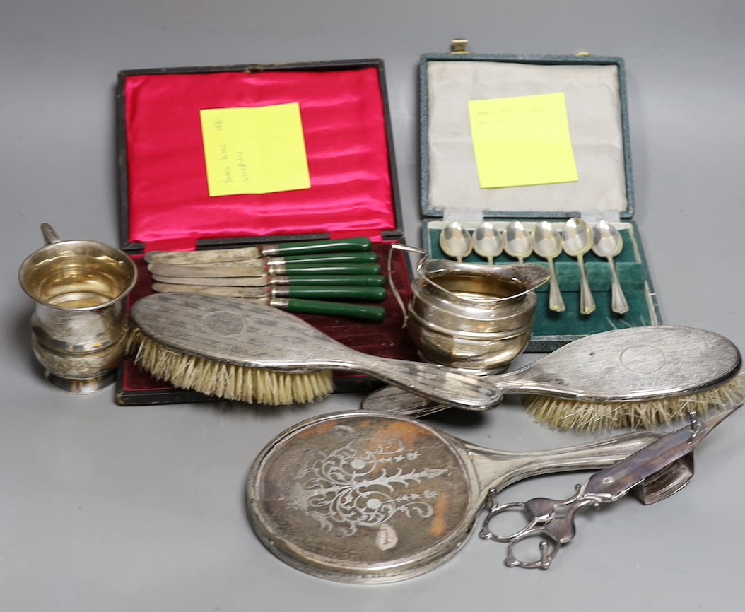 A small group of silver items including a tortoiseshell mounted hand mirror, London, 1917, two silver mounted clothes brushes, a cased set of six teaspoons, a mug and sugar bowl, together with a pair of plated candle snu